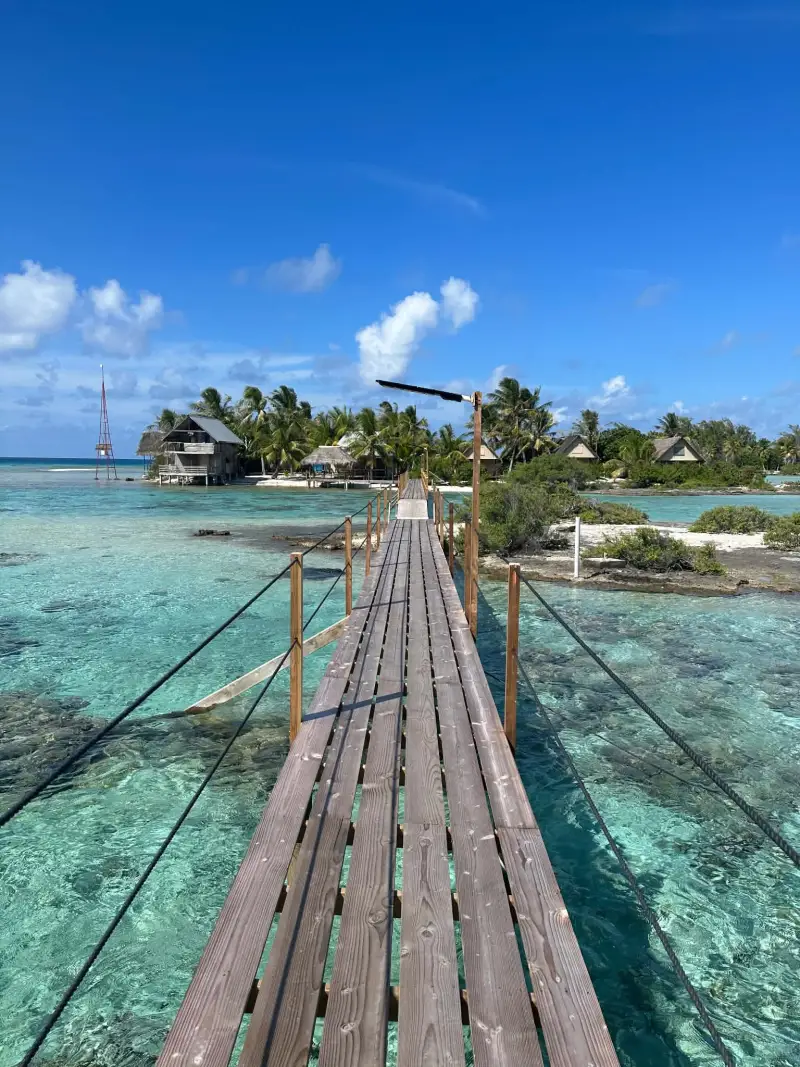 Ponton en bois au-dessus du lagon turquoise de Fakarava, vers un motu et ses fare